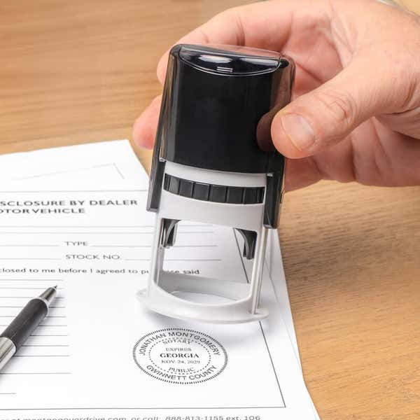 Notary tool in hand applying certification stamp on legal document surface