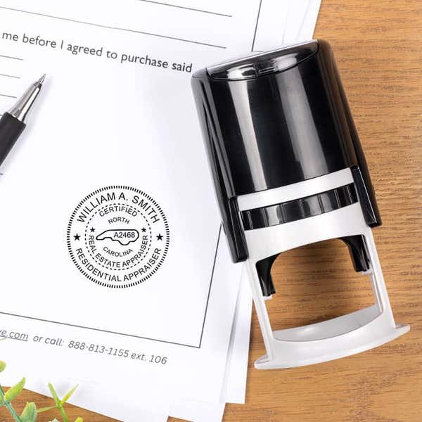 North Carolina appraiser stamp on paperwork beside a black self-inking stamp and pen on a wooden desk.