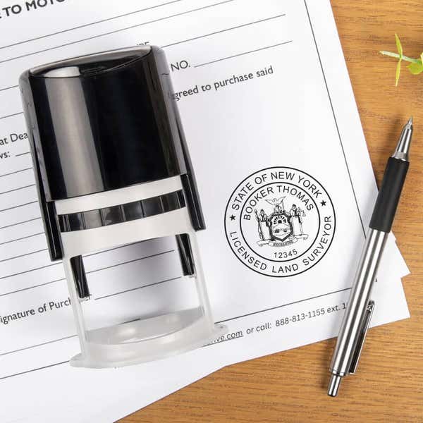 The State of New York Land Surveyor Seal at the bottom of a document with a stamp and a pen laying next to it