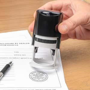 Hand presses New York notary stamp onto motor-vehicle disclosure form.