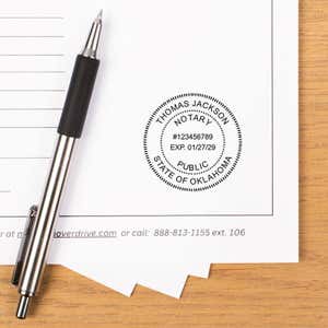 Stamped notary seal impression on a document beside a pen on a desk.