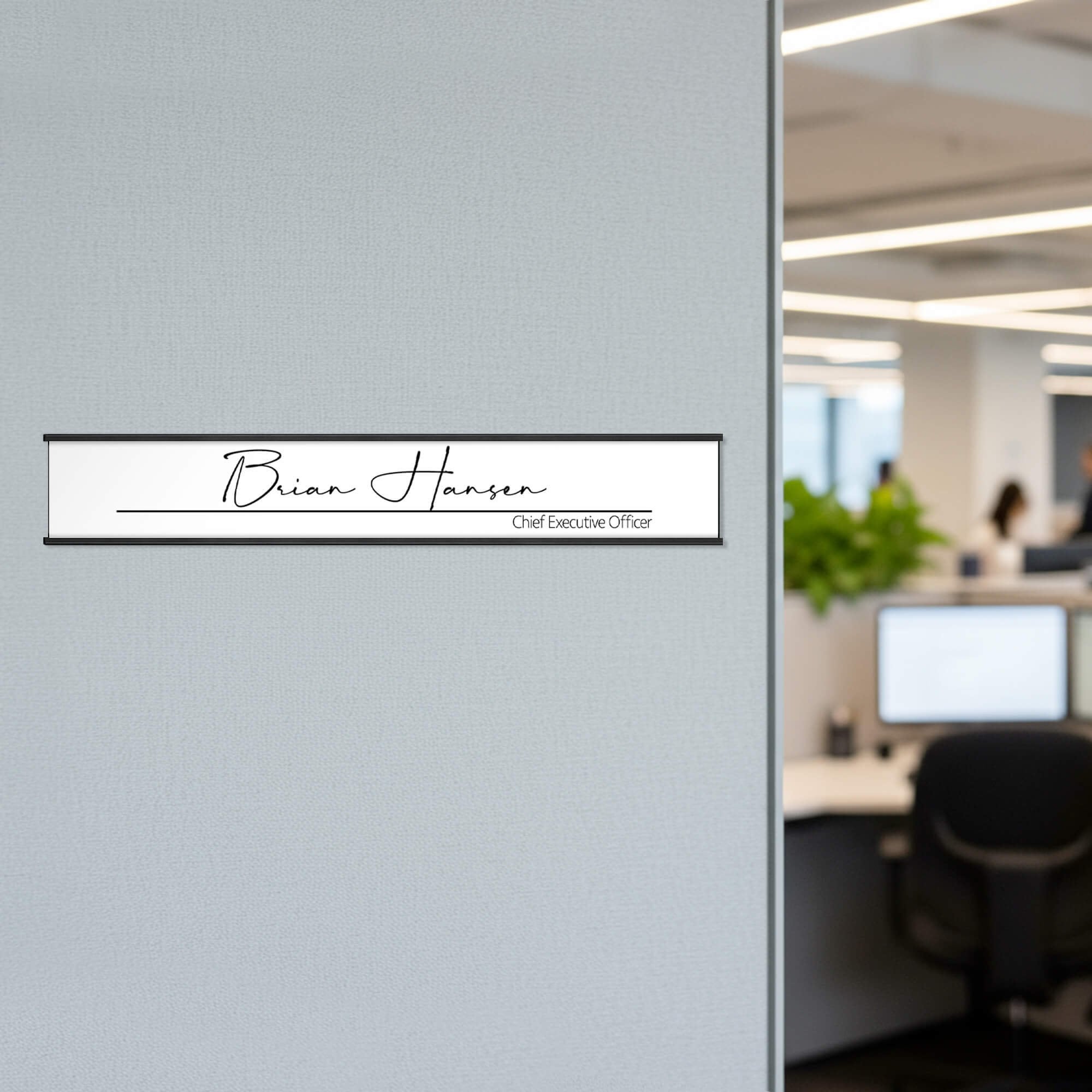 A white name plate with a black aluminum holder on an office wall A white name plate with a black aluminum holder on an office wall