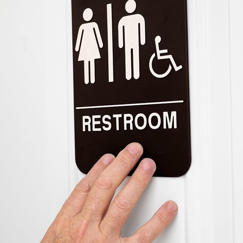 Someone feeling the braille on a 9 x 6 restroom sign Someone feeling the braille on a 9 x 6 restroom sign