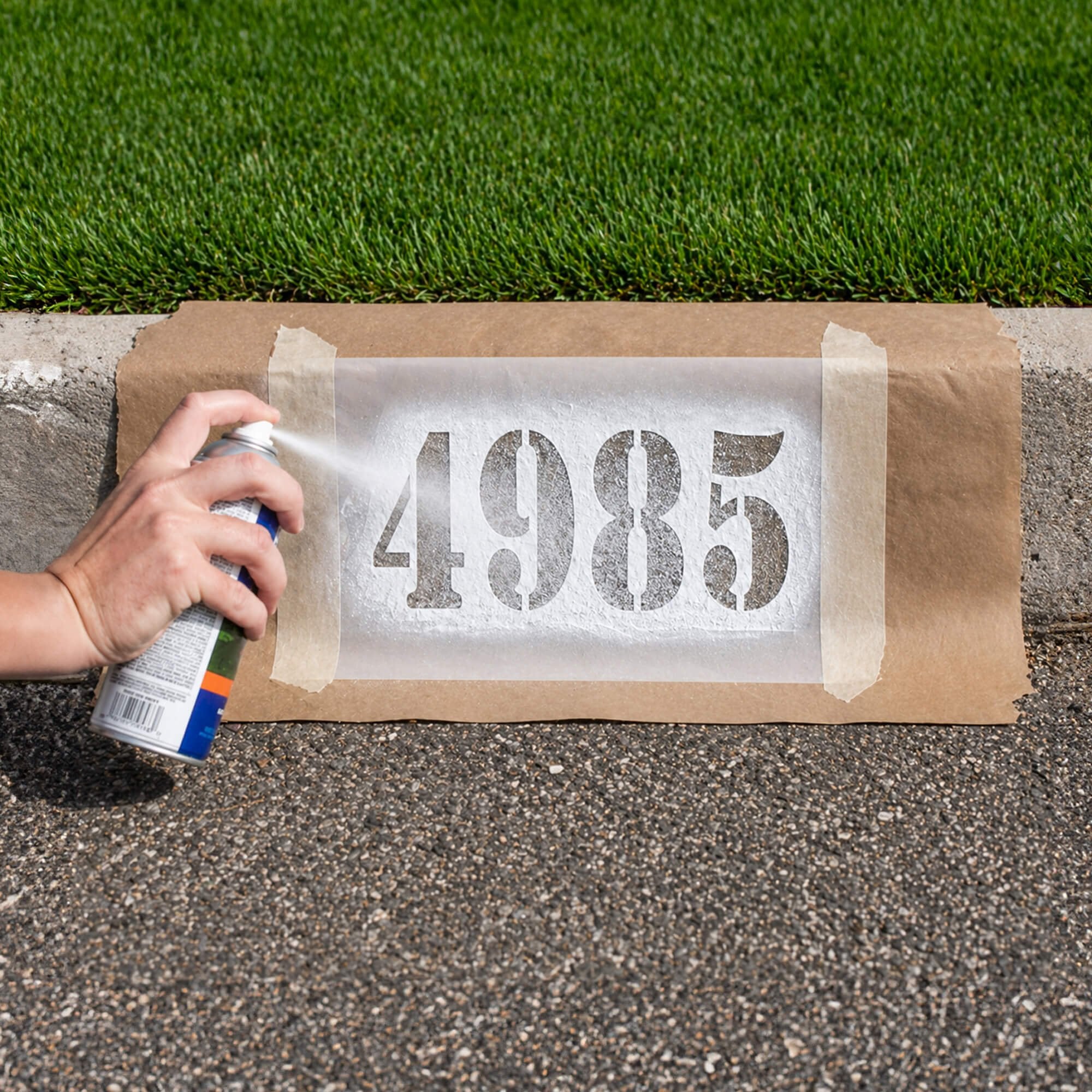A person spray painting numbers onto a curb using a stencil A person spray painting numbers onto a curb using a stencil