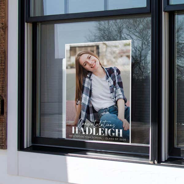 A vertical yard sign for a graduate displayed in a window