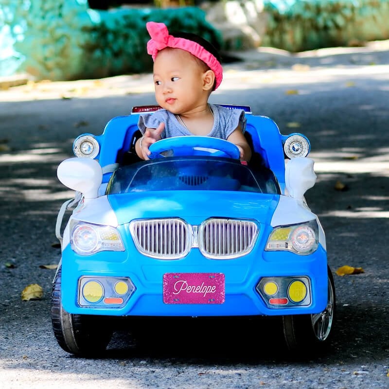 A Girl in a Blue Toy Car with a Pink Mini License Plate with Her Name