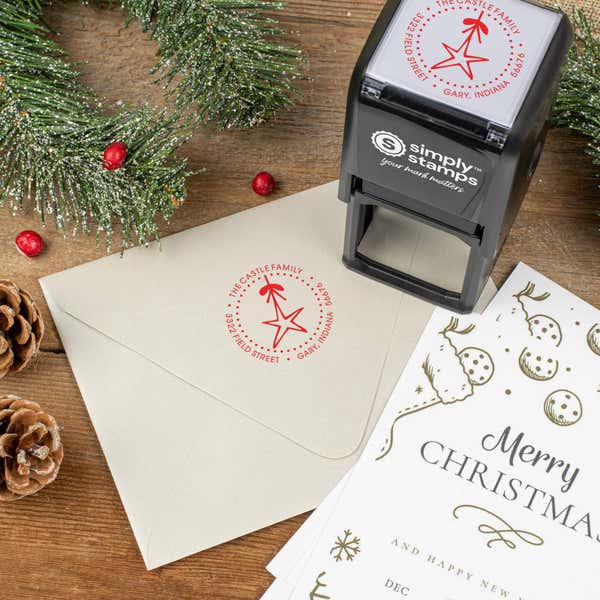 Holiday-themed ‘Holiday Star’ address stamp shown on envelopes beside festive stationery, pinecones, and decorations.