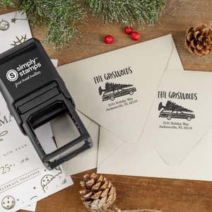 Holiday-themed ‘Griswold Holiday’ address stamp shown on envelopes beside festive stationery, pinecones, and decorations.